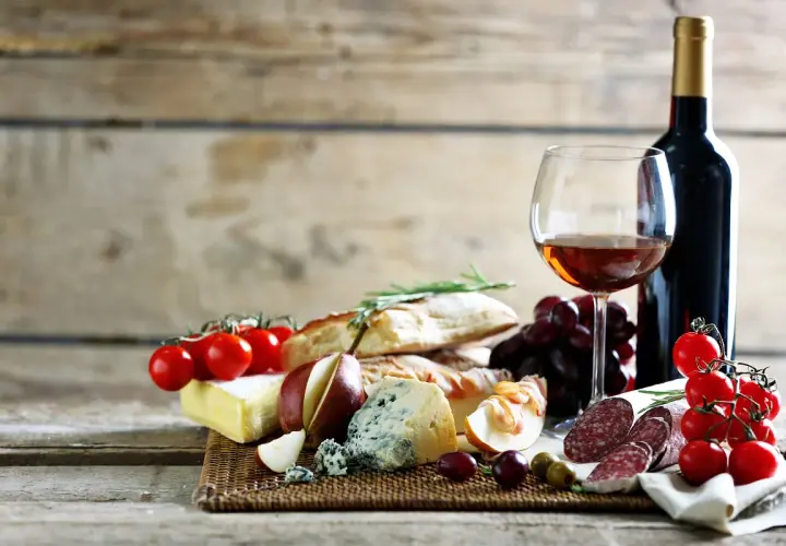 Degustacja najpopularniejszych win włoskich: kieliszek wina, butelka, sery, wędliny, pieczywo, winogrona i pomidorki.