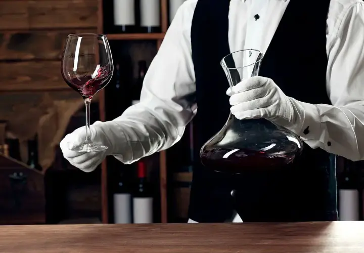 Kellner mit Handschuhen hält Weinglas und Karaffe. Eine Flasche Wein ergibt etwa 5 Gläser.