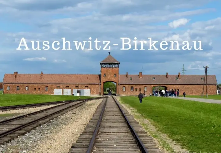 Brama obozu Auschwitz-Birkenau, gdzie jest to miejsce pamięci. Tłum zwiedzających podąża torami kolejowymi.