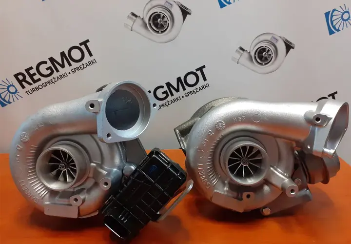 Dwa turbosprężarki, jedna z nich to hybrydowy turbo, na tle logo REG MOT.