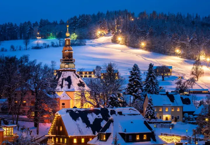 Ein verschneites Dorf in Deutschland, beleuchtet von warmem Licht. Perfekt für einen romantischen Winterurlaub.