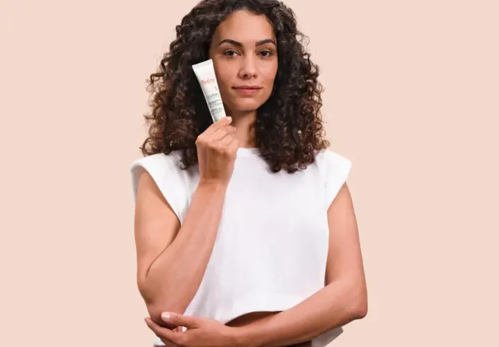 Mujer con cabello rizado sostiene un tubo de Cicalfate, crema reparadora para la piel.