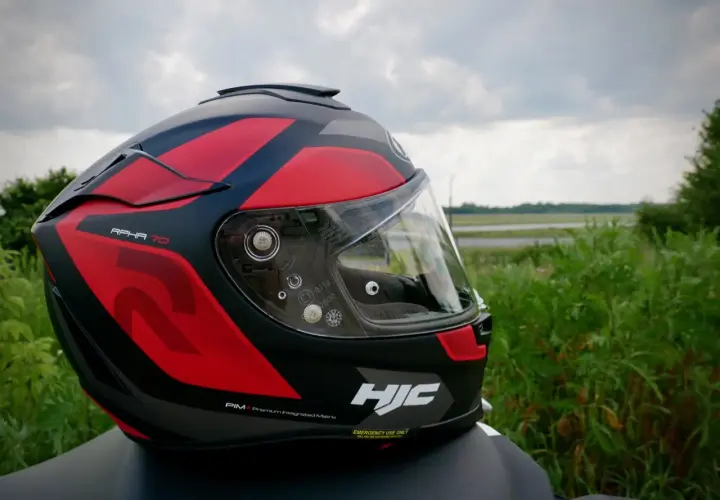 Kask motocyklowy HJC RPHA 70 w czerwono-czarne wzory, gotowy na przygodę na tle zieleni i nieba.