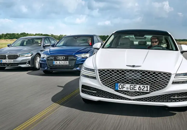 Un Genesis blanco lidera un grupo de sedanes de lujo, incluyendo un Audi azul y un BMW gris, en una carretera abierta.