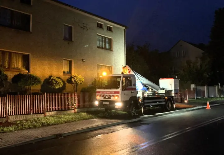 Samochód Tauron z podnośnikiem przy budynku, nocą. Zgłoszenie awarii w toku.