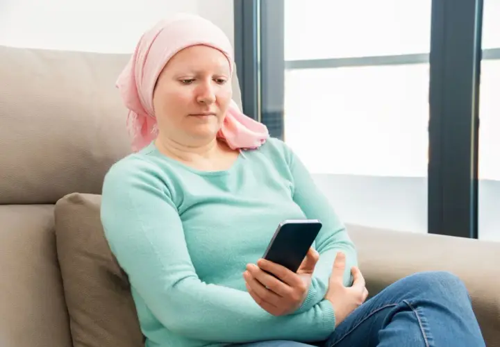 Kobieta w chustce na głowie, po chemioterapii, sprawdza telefon. Może szuka informacji o 500 plus dla chorych na raka ZUS.