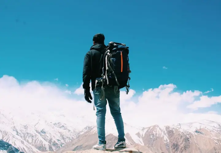 Un uomo con zaino in spalla ammira un panorama montano innevato. Il viaggiare da soli psicologia è un'esperienza di crescita.
