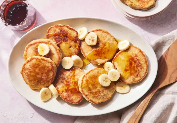 Tortitas de avena y plátano doradas, cubiertas con rodajas de plátano y sirope. Un desayuno delicioso y saludable.