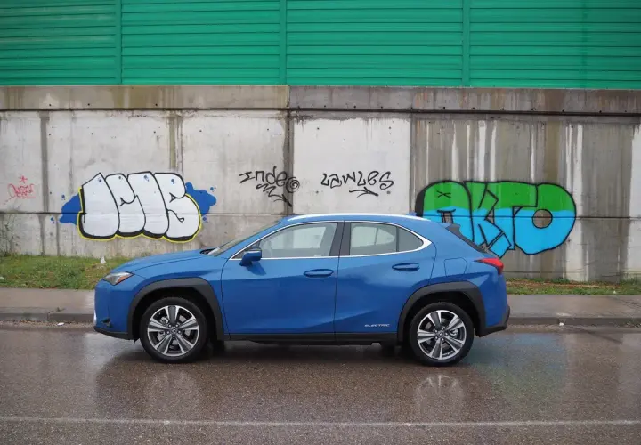 Lexus UX azul aparcado frente a un muro con grafitis. A pesar de los problemas, el coche eléctrico se ve elegante.
