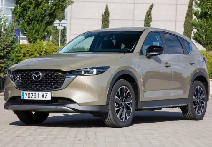 Un Mazda CX-5 2.2 150cv color bronce, con llantas negras y plateadas, estacionado en un día soleado. ¡Un coche ideal para tus viajes!