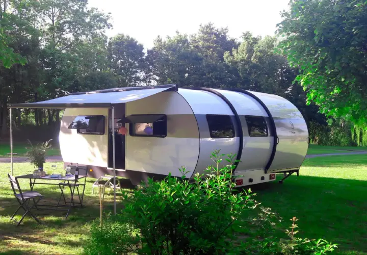 Une caravane XXL extensible, prête pour l'aventure, avec un auvent déployé et une table dressée sur l'herbe.