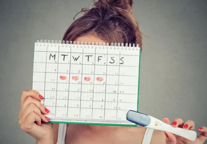 Donna con calendario segnato per il calcolo ovulazione e nidazione, tiene in mano un test di gravidanza.