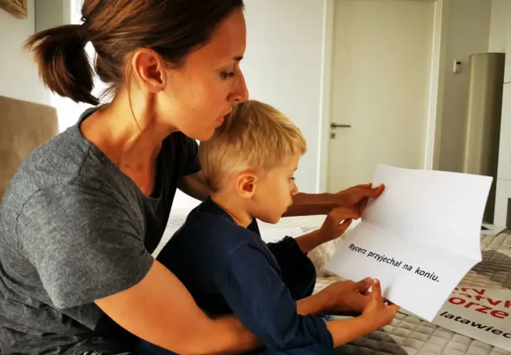 Mama uczy 5-latka czytać. Razem czytają tekst: "Rycerz przyjechał na koniu".