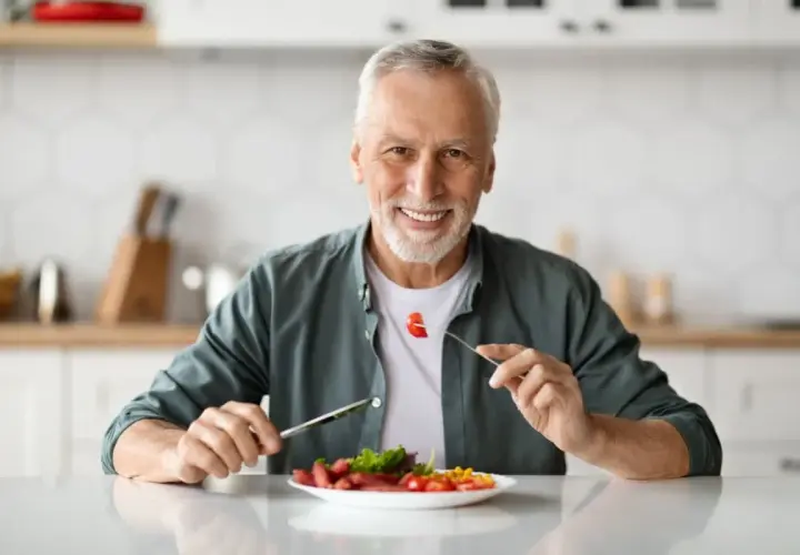 Uomo sorridente mangia cibo sano, godendosi ogni boccone con il suo impianto dentale.