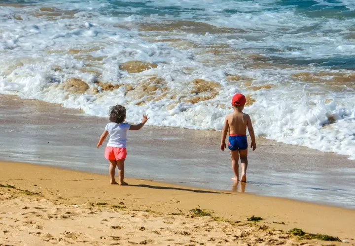 Dzieci w strojach kąpielowych dwuczęściowych dla dzieci bawią się na plaży, machając do fal.