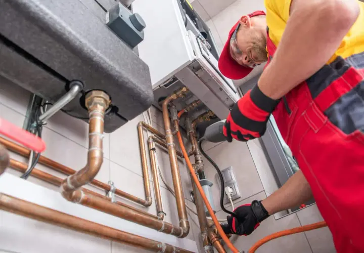 Un technicien installe une chaudière à gaz, une étape clé pour ma prime rénov. Il manipule des tuyaux en cuivre avec soin.