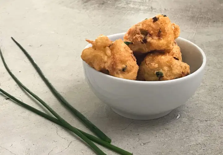Tazón blanco con buñuelos de bacalao dorados y crujientes, decorado con cebollino fresco.