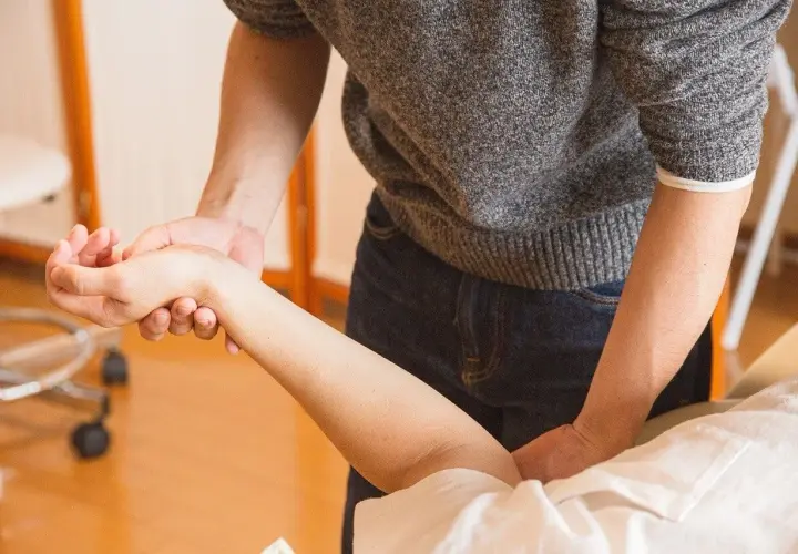 Fizjoterapeuta delikatnie masuje przedramię pacjenta, pokazując, jak leczyć łokieć tenisisty.