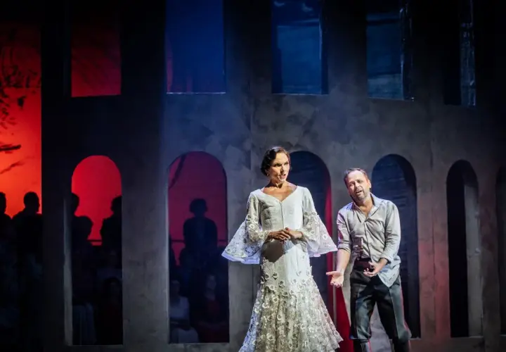 Carmen w białej sukni i mężczyzna na scenie operowej. Tło z łukami i czerwonymi światłami.