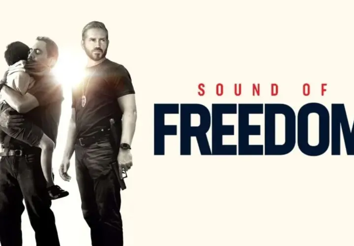 Un uomo abbraccia un bambino, mentre un altro uomo con una pistola guarda. Titolo: Sound of Freedom. Le recensioni lodano questo film.