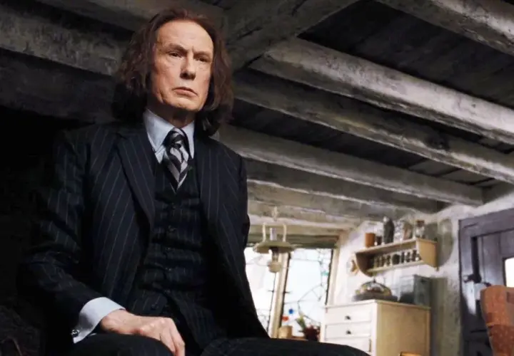 Bill Nighy jako Rufus Scrimgeour w Harry Potterze, w garniturze, siedzi w ponurym wnętrzu.