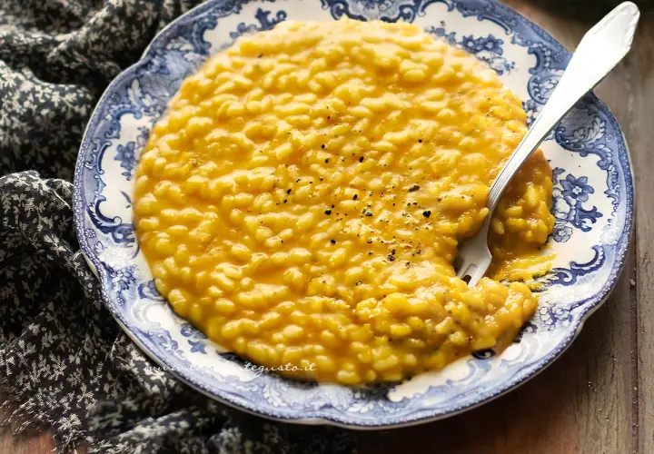 Un cremoso risotto zucca e rosmarino, servito su un piatto decorato, con una forchetta che affonda nella sua bontà.