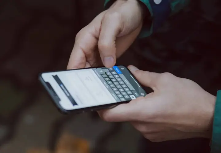 Dłonie trzymające smartfon z klawiaturą. Widoczna opcja "jak zwiększyć litery w telefonie" na ekranie.