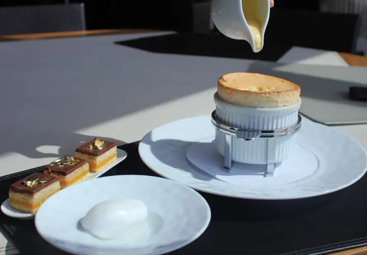 Un délicieux soufflé au Grand Marnier, encore chaud, est servi avec une crème anglaise. À côté, des petits gâteaux au chocolat et une boule de sorbet.