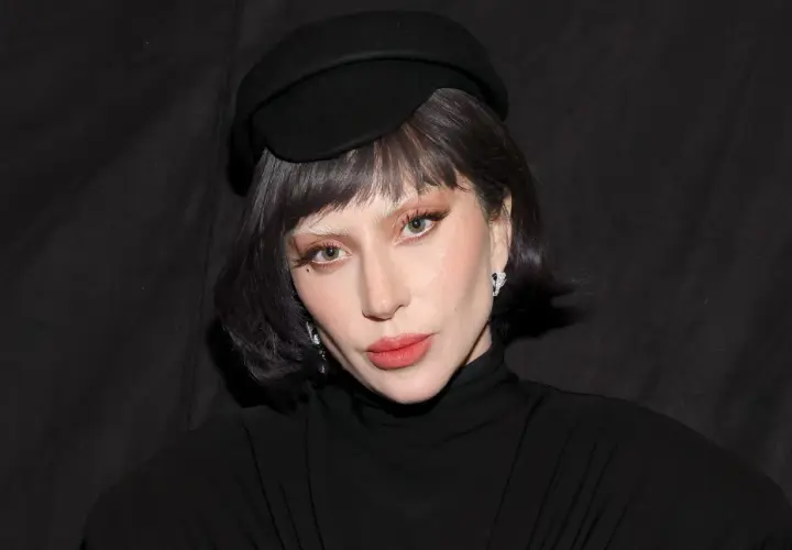 Lady Gaga w czarnym kapeluszu i golfie, z makijażem i biżuterią.