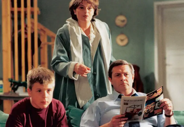 Familjen Svensson samlad i vardagsrummet. Pappa läser tidningen, mamma står och pratar, sonen sitter bredvid.