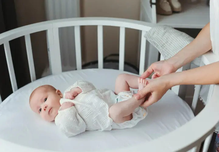 Delikatne nóżki noworodka w białej koronkowej kaftaniku, mama delikatnie je dotyka.