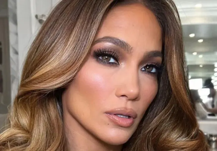 Primer plano de una mujer con maquillaje glamuroso y unos preciosos reflejos en pelo castaño que brillan con la luz.