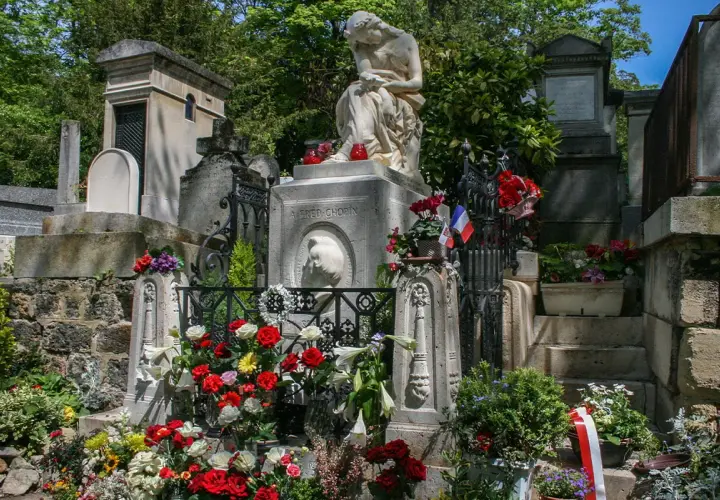 Grób Chopina na cmentarzu Père Lachaise w Paryżu, ozdobiony kwiatami i flagami.