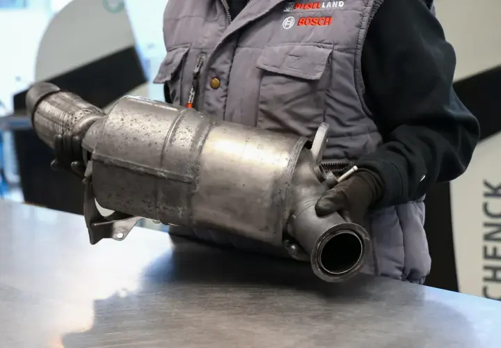 Mechanik w rękawiczkach trzyma element układu wydechowego. To część do diesla bez DPF, gotowa do montażu lub wymiany.