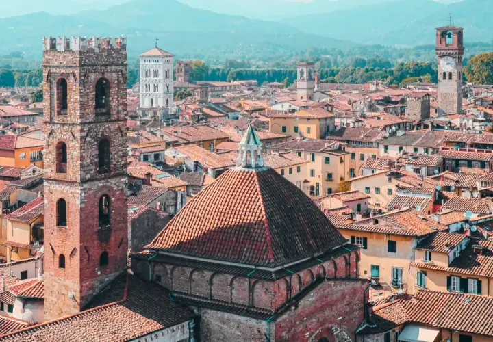 View over a walled city in Tuscany, with terracotta roofs, ancient towers, and distant mountains.