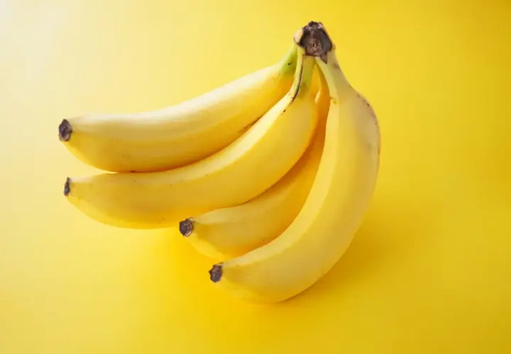 Pęczek żółtych bananów na żółtym tle. Zastanawiasz się, ile kalorii ma średni banan?
