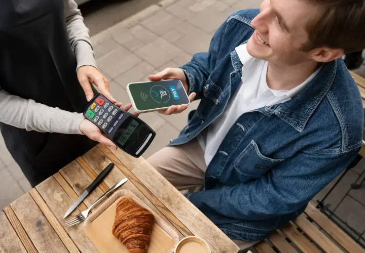 Uśmiechnięty mężczyzna płaci telefonem Santander za croissant. Szybko i wygodnie, jak płacić telefonem Santander.