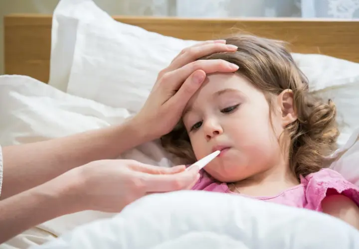 Bambina a letto con termometro in bocca, mano sulla fronte. La febbre da ansia la fa stare male.