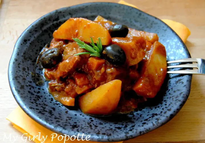 Un plat appétissant de sauté de veau à la tomate, garni d'olives noires et de romarin. Quel vin avec sauté de veau à la tomate ? Un rouge léger serait parfait.