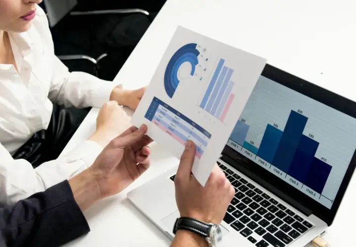 Data scientist analizuje wykresy i dane na laptopie, omawiając wyniki z kolegą.