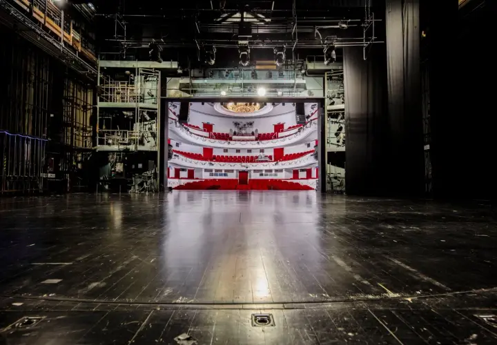 Widok na pustą widownię z czerwonymi fotelami i balkonami, widziany ze sceny. To wnętrze teatru dramatycznego w Warszawie, gotowe na spektakl.