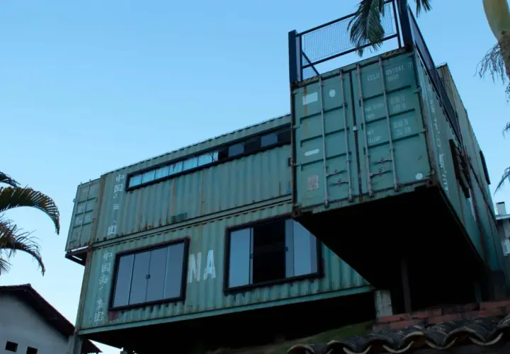 Nowoczesny dom z kontenerów, piętrowy, z dużymi oknami i tarasem na dachu.