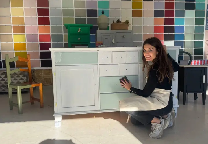 Mujer lijando un armario en proceso de pintura, con un fondo de muestras de colores.