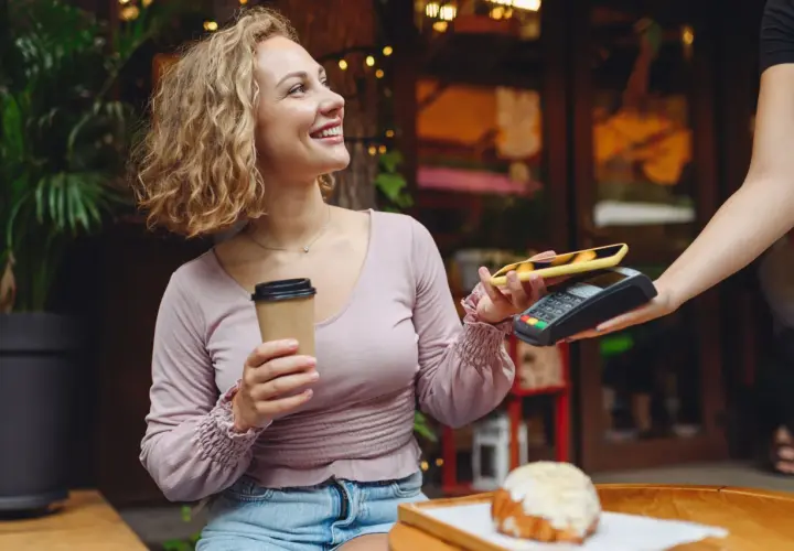 Uśmiechnięta kobieta z kawą płaci telefonem zbliżeniowo za croissant. Szybki przelew na telefon w kawiarni.