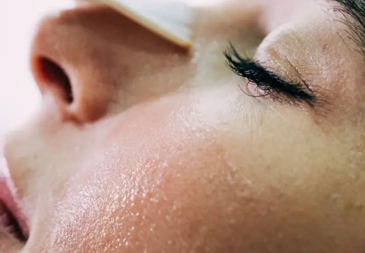 Gros plan sur une peau grêlée, humide et lumineuse, avec un œil fermé et des cils longs.