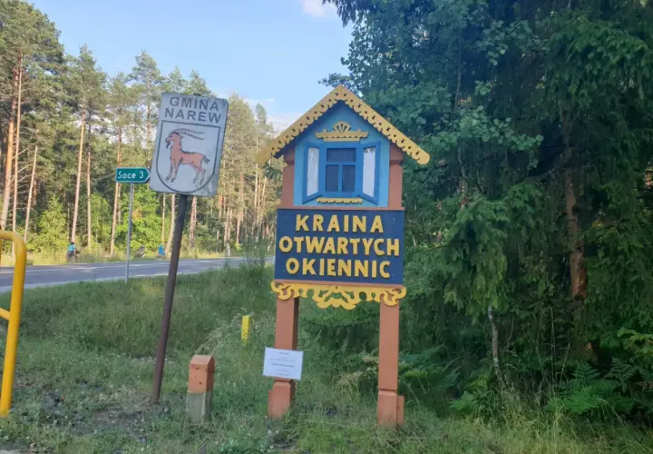Drewniana tablica wita w Krainie Otwartych Okiennic. Obok znak Gminy Narew.