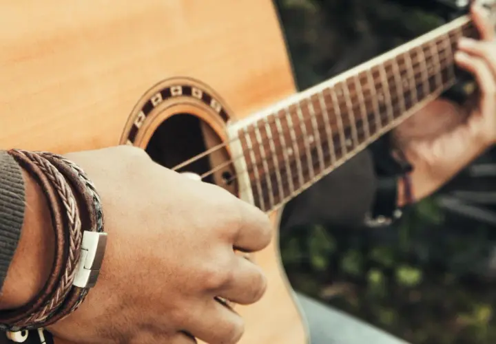 Dłoń z bransoletką gra akord d na gitarze akustycznej.