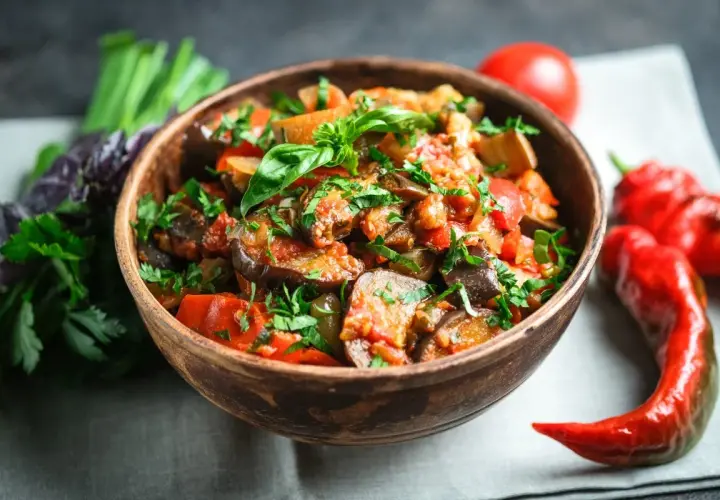 A miseczce caponata siciliana, pełna bakłażana, pomidorów i papryki, ozdobiona świeżą bazylią i pietruszką.
