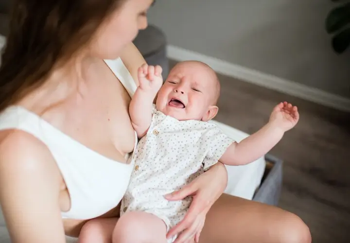 Bambino piange per la dentizione neonato rimedi. Mamma lo culla, cercando sollievo.