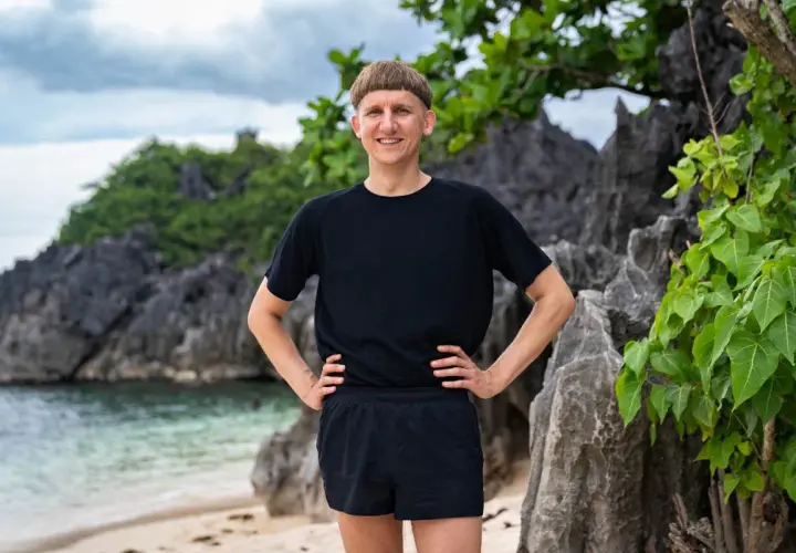 Pål Robinson står på en strand med klippor och grönska bakom sig.
